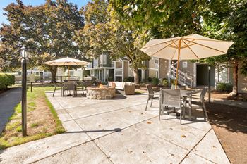 A sunny day at the park with a yellow umbrella and a fire pit.